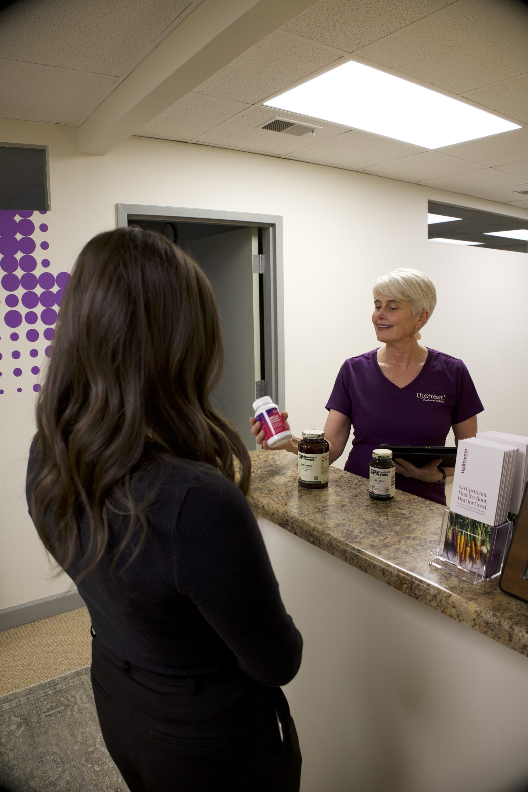 Clinician speaking with a patient at a front desk while reviewing supplements during a visit related to digestive symptoms Omaha care.