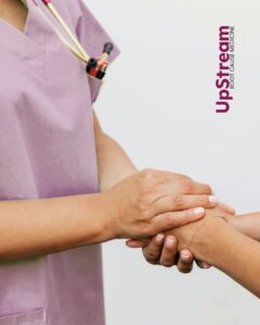 A Functional Medicine provider in Omaha wearing scrubs gently holds a patient’s hands, representing supportive, root-cause healthcare at UpStream.