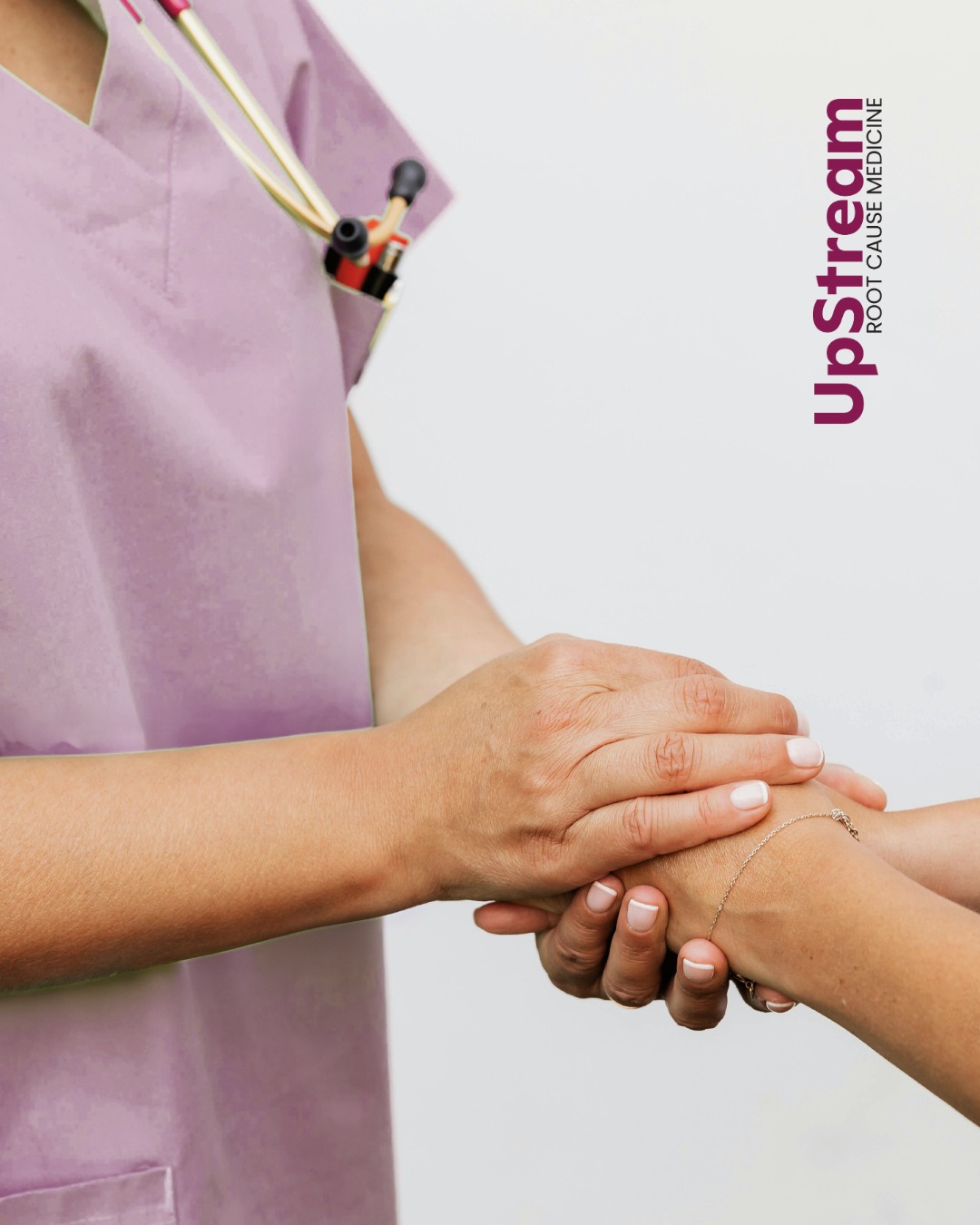 A Functional Medicine provider in Omaha wearing scrubs gently holds a patient’s hands, representing supportive, root-cause healthcare at UpStream.
